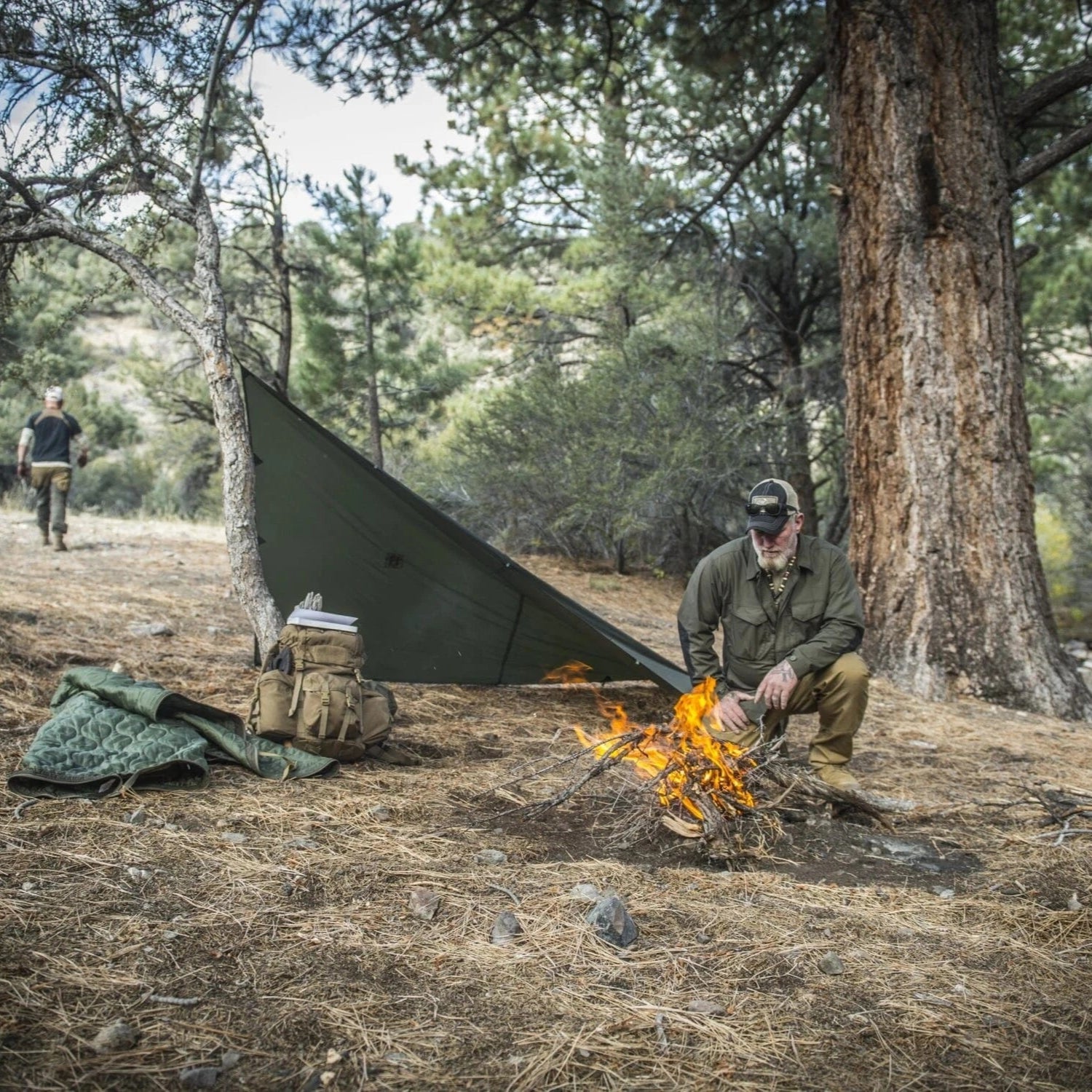 Camouflage tarp set up in forest clearing beside tactical backpack