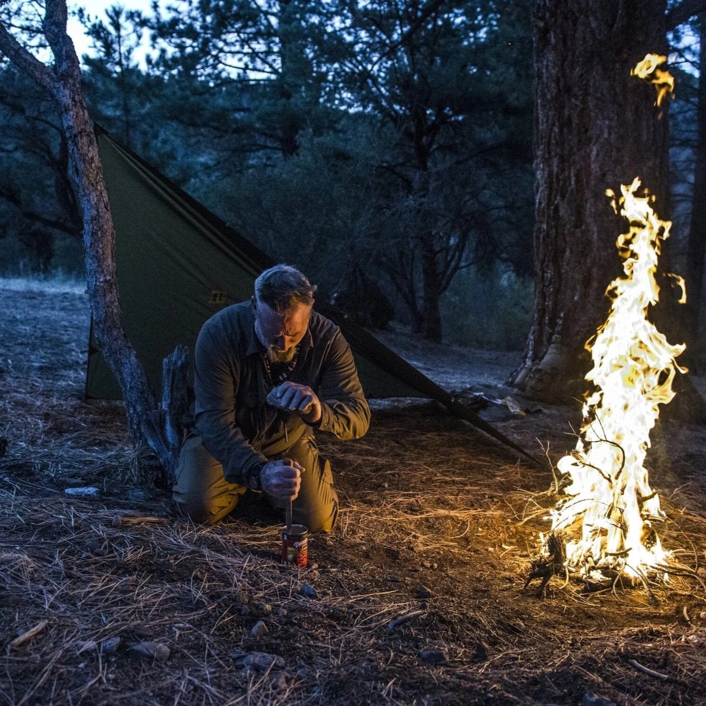 Tactical tarp shelter in forest set up near campfire at night